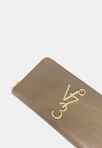 Cartera de cuero beige con acento en logo dorado, cierre de cremallera, textura suave y esquinas redondeadas. Diseño compacto para un fácil transporte.