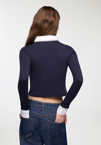 Maglietta a maniche lunghe blu navy con colletto e polsini bianchi; design attillato, texture liscia, lunghezza cropped, abbinata a jeans blu a vita alta.