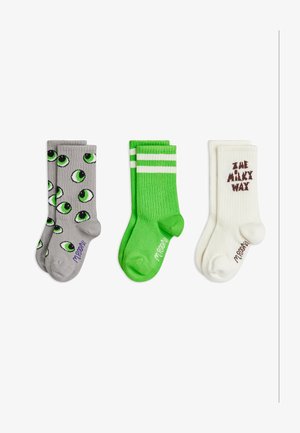 Trois paires de chaussettes de sport : grises avec des motifs d'yeux verts, vert vif avec des rayures blanches, et crème avec le texte "The Milky Way" en marron.