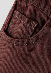 Primo piano di un tessuto denim marrone scuro che mostra due tasche cucite su pantaloni o jeans.