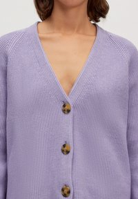 Lila gebreide cardigan met een diepe V-hals, voorzien van vier contrasterende bruine knopen aan de voorkant en een ribbelstructuur door het hele stuk.