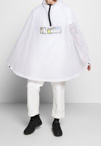 Vit huvad poncho med dragkedja fram och en reflekterande logotyp patch. Har en lös, cirkulär design och en smidig, lätt textur.