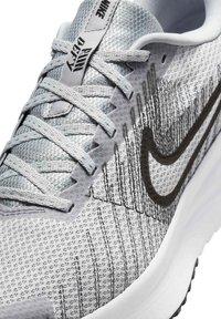 Szare buty sportowe z teksturowaną siateczką, z czarnym logo w kształcie 'swoosh', płaskimi sznurowadłami i białą, amortyzującą podeszwą.