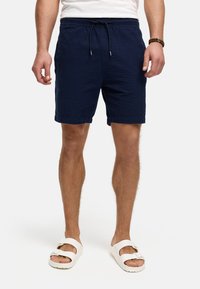 Pantalones cortos azul marino texturizados con cintura elástica y cordón. Se llevan con sandalias blancas que presentan un diseño de correa con hebilla.