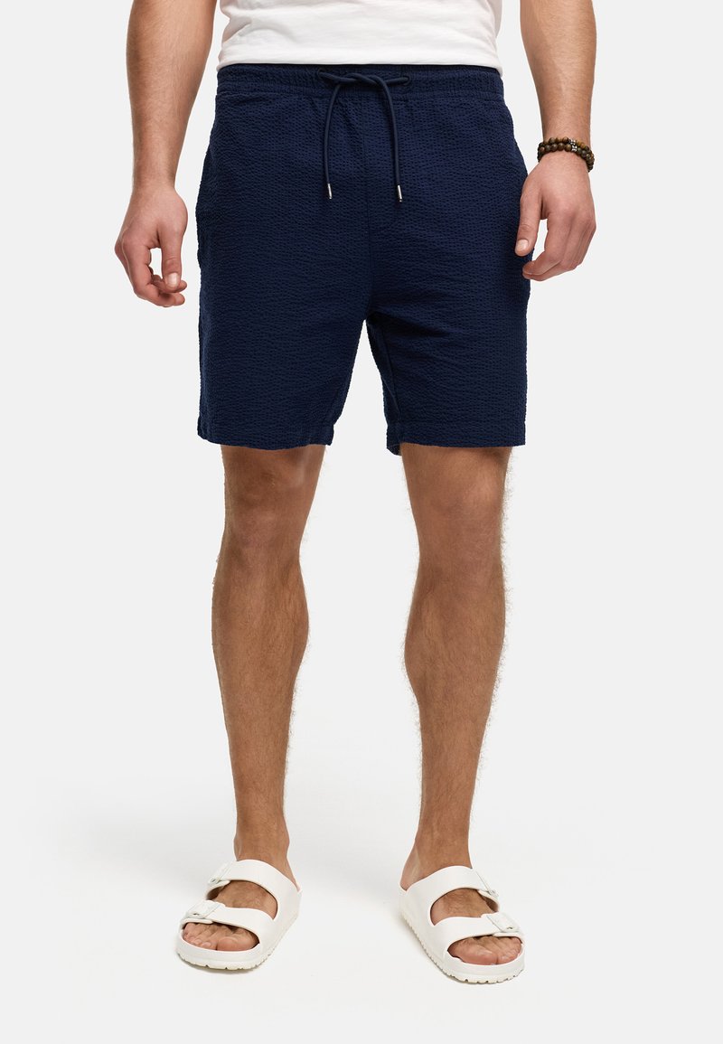 Pantalones cortos azul marino texturizados con cintura elástica y cordón. Se llevan con sandalias blancas que presentan un diseño de correa con hebilla.