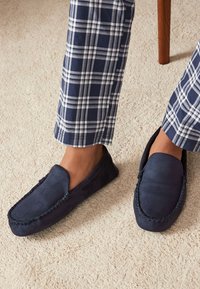 Navy blå ruskind loafers med et mokkasin-design, der har kontraststing og en glat finish, kombineret med marineblå og hvide ternede bukser.
