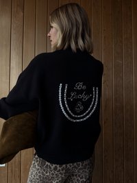 Czarny sweter o luźnym kroju z żebrowanym dołem, ozdobiony białymi koralikami układającymi się w napis "Be Lucky" oraz kwiatowym akcentem.