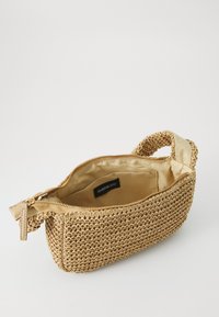 Sac tissé beige avec un extérieur texturé, fermeture éclair dorée et intérieur doublé en satin. Dispose d'une poignée robuste pour le transport.