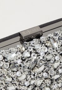 Pochette noire avec quincaillerie argentée, ornée de perles transparentes et argentées, ainsi que de perles en faux. Présente une fermeture à fermoir avec une gravure "MASCARA".