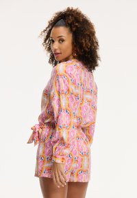 Korte mouw romper in een roze, oranje en blauwe paisleyprint. Gemaakt van lichtgewicht stof, met een strikceintuur en elastische manchetten.