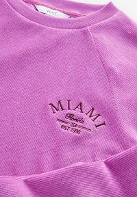 Rosa ribbad sweatshirt med rund halsringning. Har "MIAMI" broderat i mörkbrunt med dekorativa detaljer under. Mjuk textur.