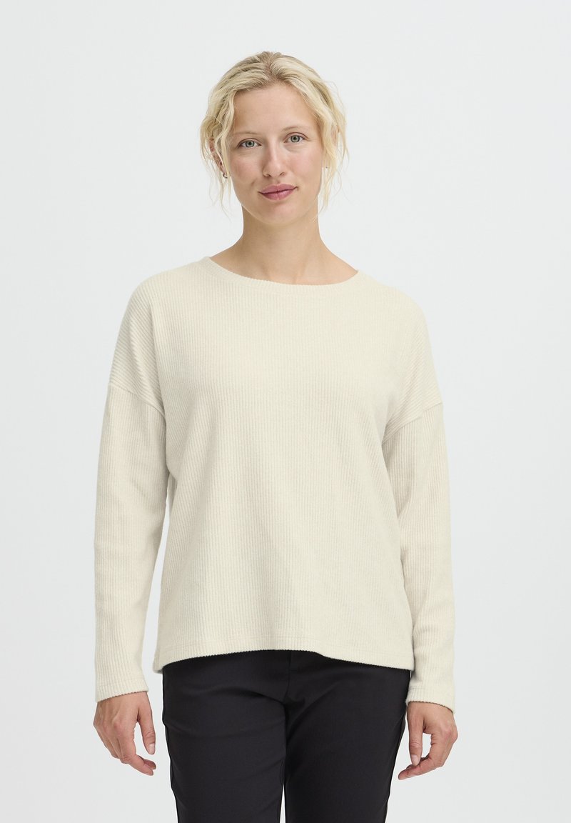 Maglione a maniche lunghe color beige chiaro a costine con scollatura ampia e vestibilità comoda. Indossato con pantaloni neri, mette in risalto una consistenza morbida e un design rilassato.