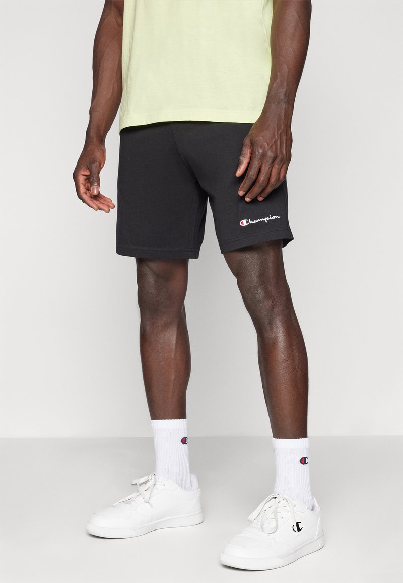 Pantalones cortos negros de mezcla de algodón, con una cintura elástica, que llegan por encima de la rodilla, y con un pequeño logo en blanco y rojo de "Champion" en el lateral.
