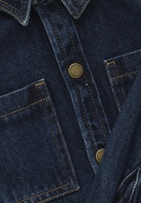 Denimskjorta i mörkblått med klassisk krage, två bröstfickor, kontrasterande sömmar och runda metallknappar. Mjukt material.