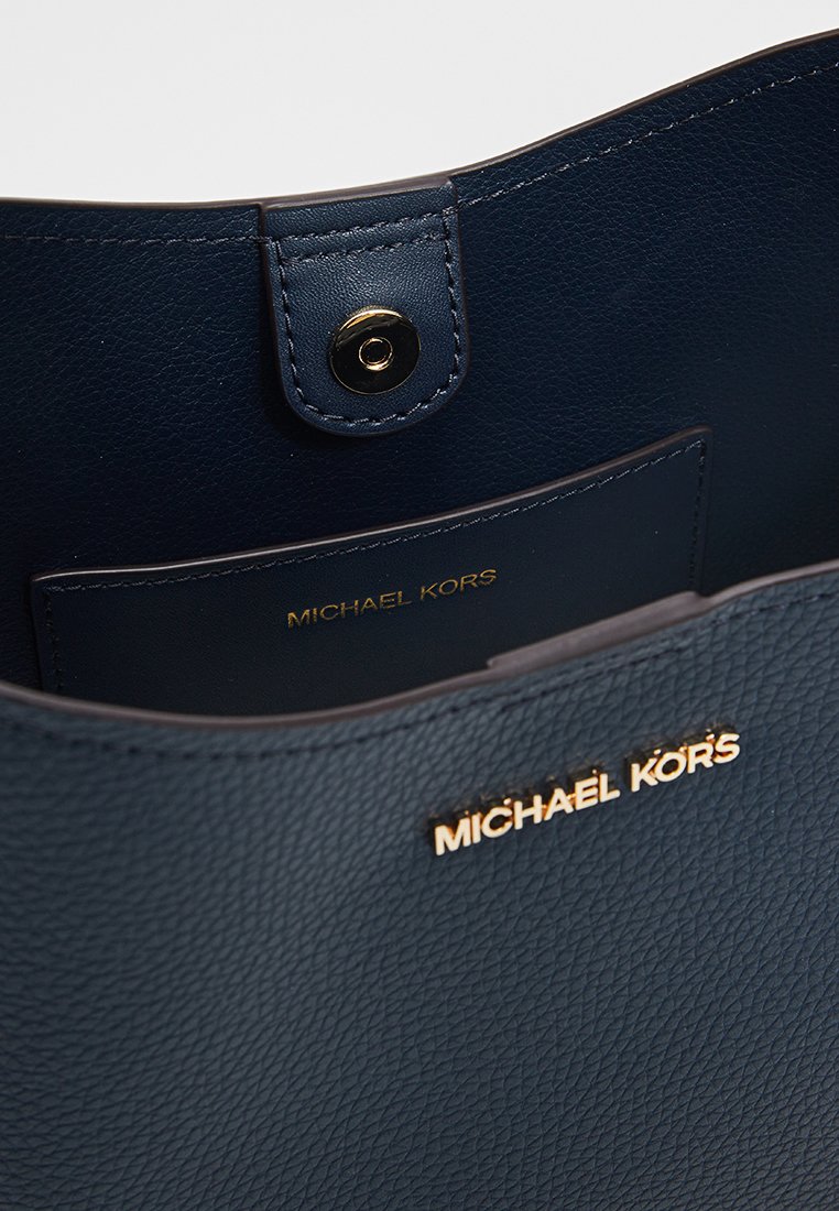 Sac en cuir granuleux bleu marine de Michael Kors avec logo doré et fermeture à pression sur la poche intérieure.