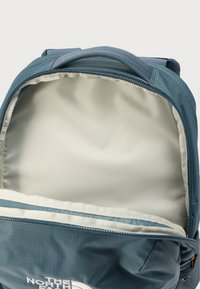 Μπλε σακίδιο με λεία εσωτερική επένδυση, κλείσιμο με φερμουάρ και λογότυπο στο μπροστινό μέρος. Διαθέτει ορθογώνιο σχήμα και ανθεκτικό υλικό.