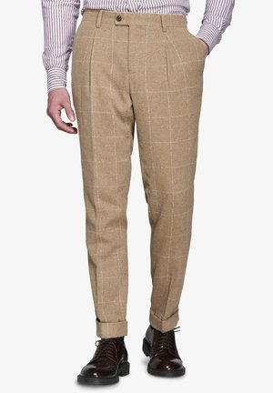 Pantalones de lana beige con un patrón de cuadros, que cuentan con pliegues delanteros, un cierre de un solo botón y dobladillos con vuelta, combinados con zapatos de cuero oscuros.