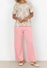 Tričko s krátkým rukávem a barevným květinovým vzorem v pastelových tónech, spárované s světle růžovými kalhotami s širokými nohavicemi a béžovými plochými botami.
