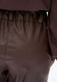 Zbliżenie ciemno-brązowych spodni skórzanych z marszczoną talią, noszonych z długim rękawem bluzki w podobnym ciemnym kolorze.