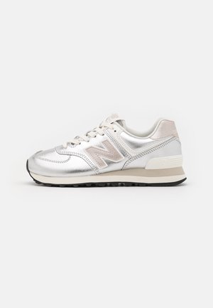Silver and beige New Balance sneaker with suede "N" logo, lace-up front, and white cushioned sole on a light background.