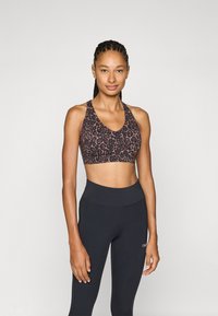 Sostén deportivo de estampado de leopardo en marrón y negro, con un escote pronunciado y tirantes anchos, combinado con leggins negros de cintura alta.