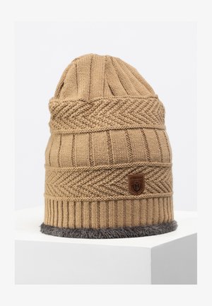 Cappello lavorato a maglia beige con un design a coste, dotato di un logo in pelle marrone e un bordo in pelliccia sintetica grigia nella parte inferiore.