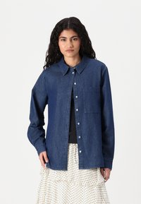 Jeansskjorta i mörkblått med knäppning fram, klassisk krage, långa ärmar, bröstficka och slät textur.