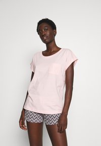 Lichtroze katoenen T-shirt met een ronde hals en korte, opgerolde mouwen, gecombineerd met zwart-witte shorts met een zigzagpatroon.