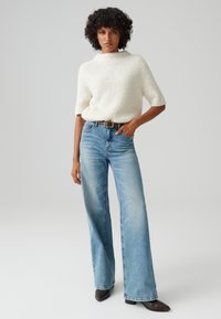 Maglione bianco a maglia testurizzata con maniche corte, abbinato a jeans a gamba larga blu chiaro e stivaletti neri con punta a punta.