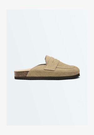 Béžový semišový nazúvací mule s korkovou stielkou a čiernou rebrovanou gumovou podrážkou, s prešitým popruhom na hornej časti.