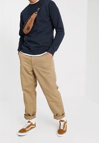 Laivastonsininen collegepaita, vaaleanruskeat chinos-housut käännetyillä lahkeilla, ruskea vyölaukku, valkoiset sukat ja ruskeat Vans-tennarit valkoisin yksityiskohdin.