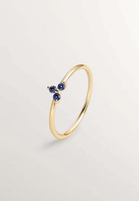 Anillo de oro con tres piedras preciosas azules dispuestas en un conjunto. Banda lisa con un acabado pulido.