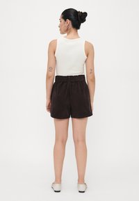 Brown corduroy shorts with a belted waist, featuring a smooth texture and a relaxed shape, paired with a sleeveless white top.