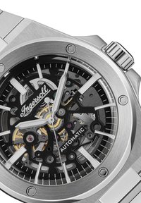 Zilveren roestvrijstalen automatiche horloge met een zwarte skeleton wijzerplaat, zilveren wijzers en uurmarkeringen. Beschikt over een gestructureerde bezel en kroon.