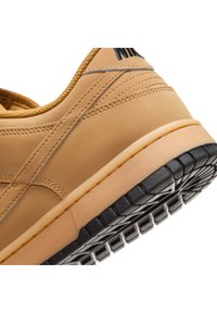 Baskets Nike couleur fauve avec semelle en caoutchouc noire, coutures détaillées et col rembourré, vues depuis un angle bas arrière.