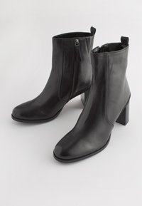 Bottes noires en cuir à talon carré, avec une fermeture éclair centrale, texture lisse et détails de couture minimalistes.