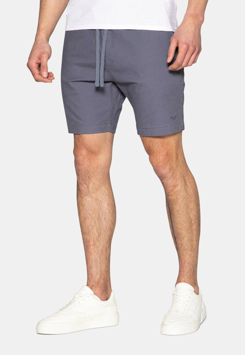 Pantaloni grigi con vita elastica e cordoncino, caratterizzati da un sottile dettaglio del logo, abbinati a sneaker bianche. Tessuto liscio.