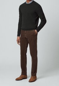 Suéter de punto acanalado verde oscuro, pantalones de pana marrón y botas de ante marrón. El conjunto presenta un cuello de camisa de rayas debajo.