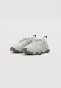 Zapatillas deportivas de color gris claro con paneles de malla y suela texturizada, que cuentan con un diseño de cordones y un tirador en el talón para facilitar su uso.
