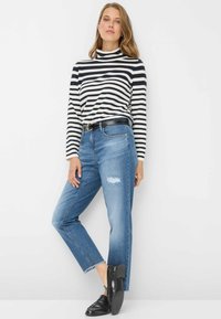 Maglia a collo alto a righe a maniche lunghe in blu navy e bianco, abbinata a jeans blu consumati e scarpe slip-on nere con tacco spesso.