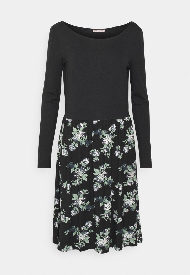 Long-sleeve dress with a black top and a flared floral skirt featuring white and green flowers on a black background. Smooth fabric texture.