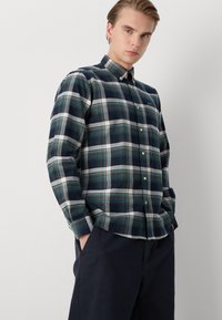 Tengerészkék kockás ing zöld és fehér kiegészítőkkel, gombos nyakkal, hosszú ujjakkal és laza fazonnal. Pamut keverék anyag, texturált szövés.