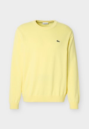 Pull jaune à manches longues avec col rond, poignets et ourlet côtelés, arborant un petit logo crocodile vert sur le côté gauche de la poitrine.