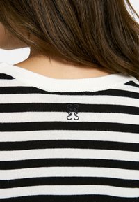 Black and white striped knit sweater with a ribbed neckline, featuring an embroidered logo on the upper back. Soft and lightweight fabric.