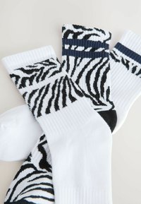 Tri par socks: bijele sa crnim zebrinim prugama, rebrasta tekstura, a jedan par ima plave pruge na vrhu.