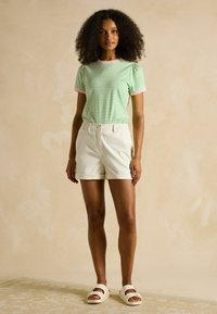 Light green and white striped short-sleeve t-shirt with pink accents, paired with cream-colored, rolled hem shorts and white slide sandals.
