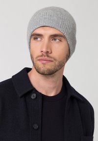 Chapeau en tricot côtelé gris, en laine douce, au design ajusté, porté avec une veste sombre dotée de boutons noirs et d'un col rond.
