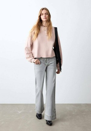 Lichtroze cropped sweatshirt met lange mouwen, gecombineerd met grijze, hoog getailleerde wijde broekspijpen jeans met decoratieve stiksels en strakke zwarte laarzen.