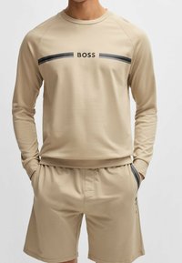 Chemise beige à manches longues et short assorti avec un accent à rayures noires et le logo "BOSS" sur la poitrine. Tissu doux et décontracté avec une coupe confortable.