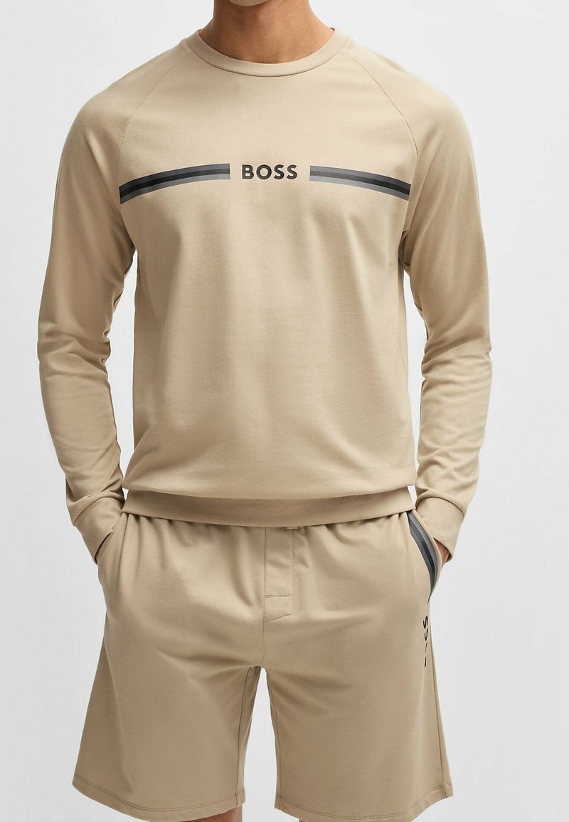 Chemise beige à manches longues et short assorti avec un accent à rayures noires et le logo "BOSS" sur la poitrine. Tissu doux et décontracté avec une coupe confortable.